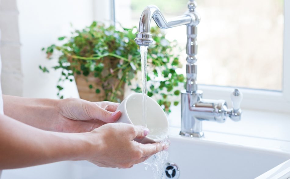 dłonie osoby myjącej filiżankę w centralnej ciepłej wodzie