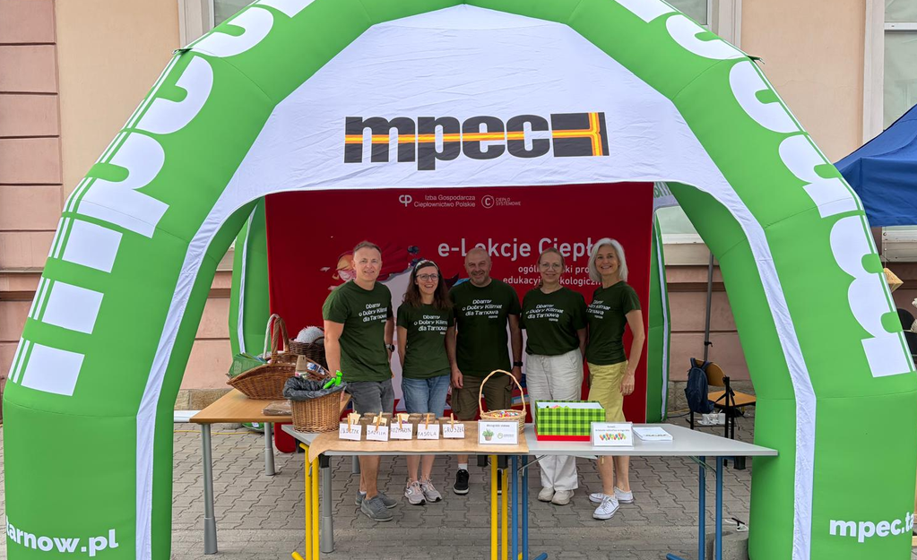 Pięcioro pracowników MPEC Tarnów w zielonych koszulkach z napisem "Dbamy o dobry klimat dla Tarnowa" na stoisku promocyjnym MPEC Tarnów zorganizowanym podczas pikniku Biblioteczna Odyseja.